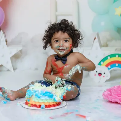 A wonderfully messy moment from a 'Pastel Rainbow' cake smash. This captures the happy chaos that makes these first birthday photoshoots so special.