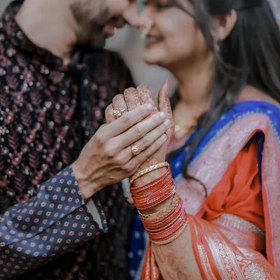 A close-up shot focusing on the couple's hands, showcasing the bride-to-be's intricate henna and colorful bangles. A beautiful detail from a Maharashtrian engagement.