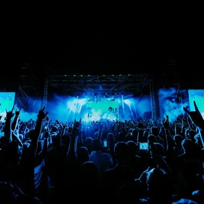 The view from the pit. A sea of fans with their hands in the air, bathed in blue light during the Dream Theater 40th Anniversary Tour. This is the community and energy of a live metal show.