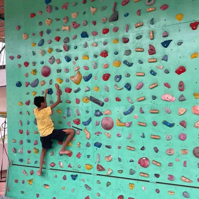 Here, a young climber navigates a bouldering route on our wall. We encourage kids to find their own path, focusing on the process of problem solving and building focus rather than just reaching the top.