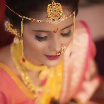 A detailed close-up of a Maharashtrian bride, focusing on the traditional 'mundavalya' (forehead ornament), expressive eye makeup, and a classic nath.