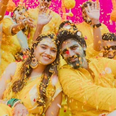 A Haldi ceremony that's a true explosion of joy! This shot captures the couple and their friends mid-celebration, covered in turmeric and flower petals, with pure happiness on their faces.