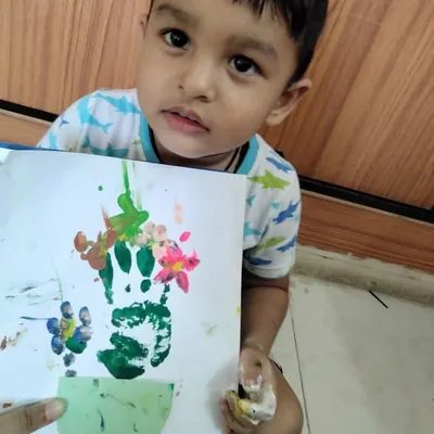 A happy student showing off his handprint flower pot painting. Art and craft activities like this are not just for fun; they help develop fine motor skills, color recognition, and a child's creative expression.