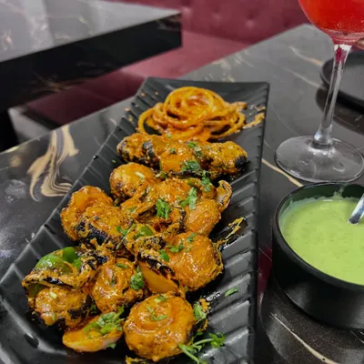 A beautifully plated dish of tandoori mushrooms. The dark plate makes the colors of the dish and the green chutney pop, and the overhead angle shows off the presentation.