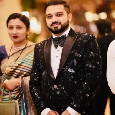 A client looking dapper in a custom black tuxedo. The jacket is adorned with intricate cut dana beadwork in black, green, and blue, creating a glittering, designer feel perfect for a reception.