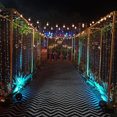 A mesmerizing entranceway for an evening event. The passage is lined with golden frames wrapped in fairy lights, with a modern chevron pattern carpet leading guests into the venue.