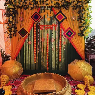 This is a classic Haldi decoration, rich with tradition. I used layers of yellow and green drapes, decorative hangings, and a large brass urli for the main ceremony, with glittery umbrellas adding a fun, festive touch.