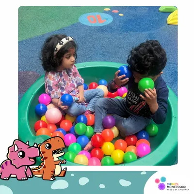 Two friends share a moment in the ball pit. This is more than just play; it's an opportunity for sensory exploration, color recognition, and developing social skills like sharing and communication.