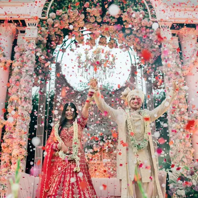 A moment of pure triumph and celebration. As confetti rains down, the couple raises their hands, united and joyful, under a magnificent floral mandap.