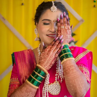 A shy and beautiful smile from a bride during her wedding ceremony. Her hands, adorned with intricate henna and green bangles, frame her face, highlighting the traditional details and her joyful expression.