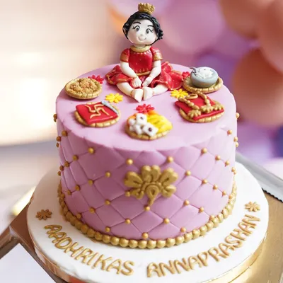 The details matter. This custom cake was designed for Aadhrika's Annaprashan, featuring a figurine of the baby and edible symbols representing elements of the traditional ceremony.