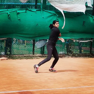 A junior girl hits a focused backhand during an AITA U-14 tournament match, demonstrating proper form and concentration.