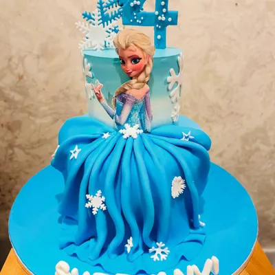 A stunning Frozen-themed doll cake featuring Queen Elsa. The bottom tier is an elaborate gown made of blue fondant, complete with edible snowflakes, making it a showstopper for a 4th birthday.