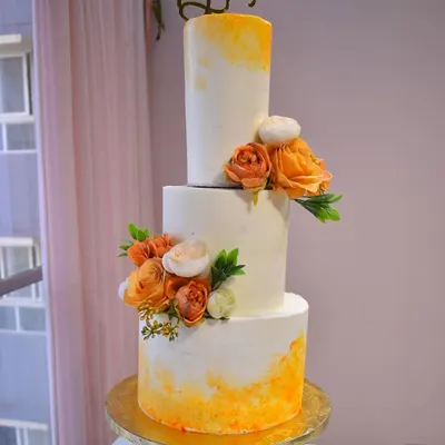 A stunning three-tiered wedding cake with a warm orange watercolor effect and delicate floral arrangements. This design combines modern artistry with timeless elegance for a truly special day.