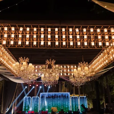 A massive, custom-built chandelier made of hundreds of individual lights serves as a dramatic overhead installation for a Sangeet-style corporate party. Below, the LED stage is ready for performances.