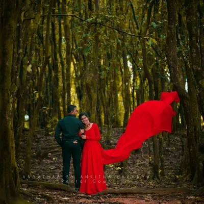 My rental red gown looks absolutely magical in this pre-wedding shoot. The long, flowing trail creates a dramatic effect against the lush green forest background, making for a truly cinematic photo.