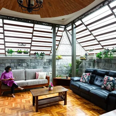 The living area in the Pioneer Lake residence is designed to feel like a sunroom. The slatted skylight roof floods the room with diffused natural light, highlighting the herringbone pattern of the reclaimed wood floor and the texture of the natural stone wall.