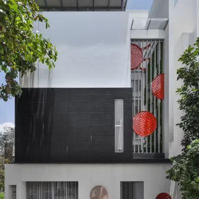 The elevation of Dr. Harsha's home reflects its minimal interior, with a monochromatic theme punctuated by a pop of red. The design features a prominent black stone-clad section and a triple-height courtyard screen.