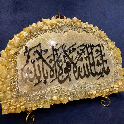 This unique semi-circular 'Mashallah' frame is a beautiful piece for a tabletop or shelf. It features black calligraphy on a grey and gold background with a textured, geode-style border.