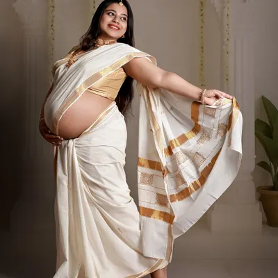 A joyful portrait of a mom-to-be showing off her baby bump in a classic white and gold Kerala saree.