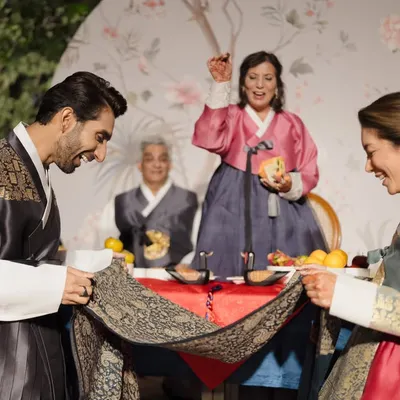 A joyful moment from a Korean Paebaek ceremony I planned, where the couple uses a cloth to catch dates and chestnuts thrown by their elders, symbolizing blessings for a fruitful life.