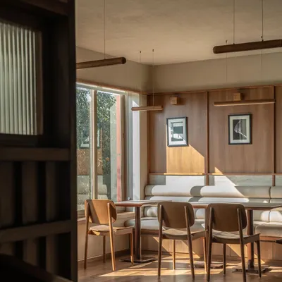 A sunlit corner in QBF Coffee, where the Japandi aesthetic comes to life. The warm wood paneling, clean lines of the furniture, and soft, natural light create a tranquil and inviting atmosphere, perfect for a quiet coffee or focused work.