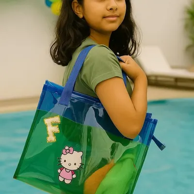 A young girl by the pool with her custom jelly tote bag. The transparent green and blue bag is personalized with her initial 'F' and a Hello Kitty patch, making it a stylish and fun accessory.