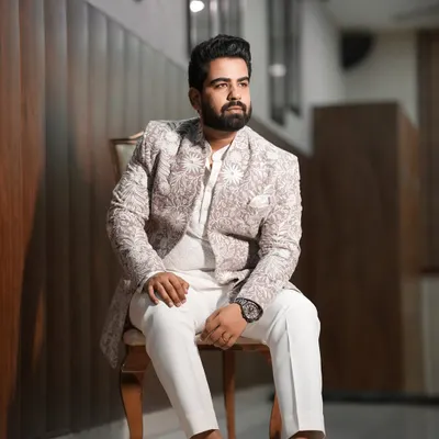 A sharp and stylish portrait of the groom seated in a chair. This shot captures his confidence and the intricate details of his embroidered sherwani before the main event.
