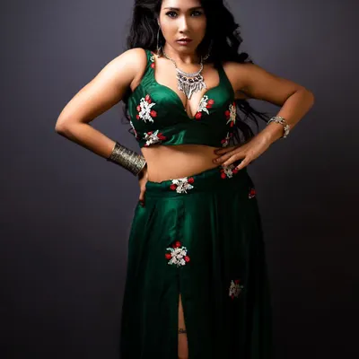 A full-length view of a custom green lehenga set. This modern ethnic piece features a deep-V crop top and a matching skirt with red and white floral embroidery, paired with bold silver jewelry.