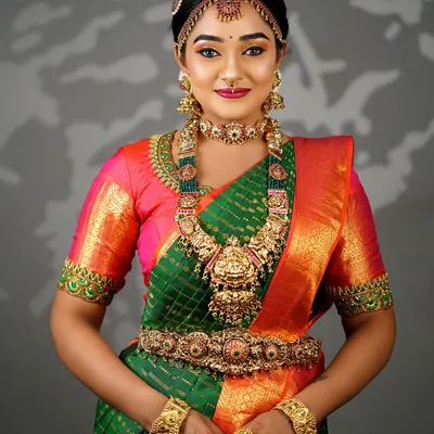 A complete South Indian bridal look featuring a green and orange Kanjeevaram saree. The makeup is designed to be waterproof and long-lasting, complementing the heavy temple jewellery.