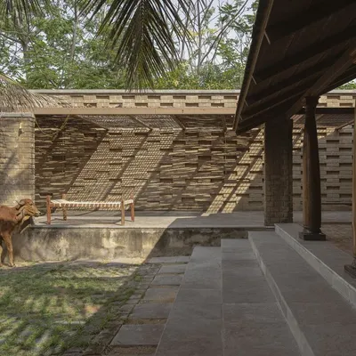 The Kaattu Veedu guesthouse, nestled in the landscape of Hosur, is designed to be in constant dialogue with its surroundings. Here, a local resident seems to agree, finding shade by the patterned earth block walls and traditional stone steps.