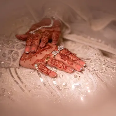 A close-up of the bride's hands, adorned with intricate mehndi and sparkling rings, resting on her embellished gown. These details are a beautiful part of her story.