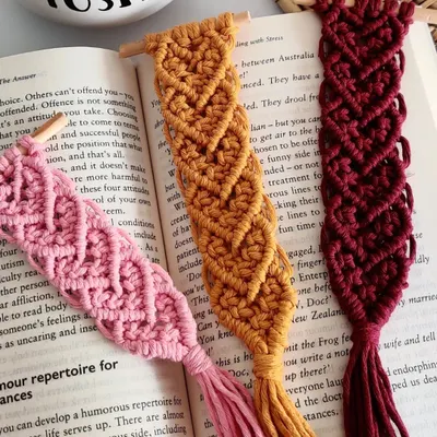My heart pattern macrame bookmarks, available in pink, mustard, and maroon. These are attached to a small wooden dowel and have a tassel at the end.