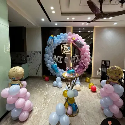 A full room view of a gender reveal or baby shower setup. The pink and blue balloon ring is the centerpiece, complemented by balloon columns topped with baby-shaped foil balloons.