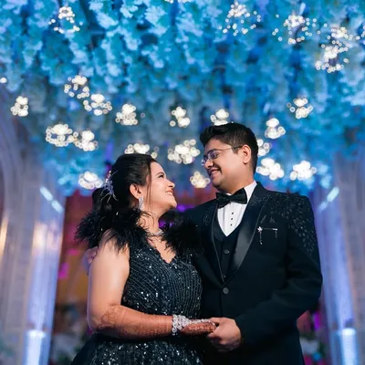 A glamorous engagement portrait with a modern fairytale feel. The couple looks stunning in their formal wear under a ceiling of blue flowers and lights.