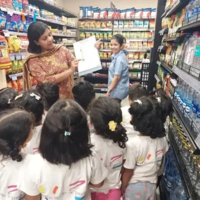 A teacher explains a shopping list to children during a field trip to the supermarket. This real-world experience teaches them about planning, budgeting, and community helpers.
