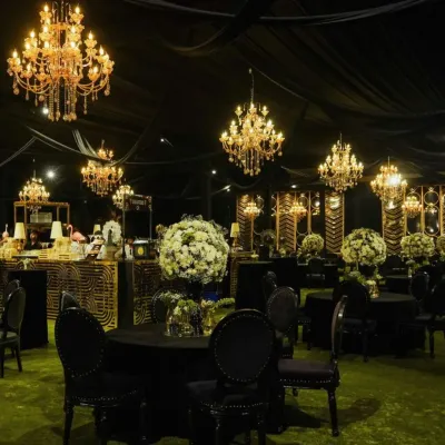 A luxurious black-themed cocktail party setup. The decor features black tablecloths, grand crystal chandeliers, and large white floral centerpieces, creating a bold and sophisticated ambiance.