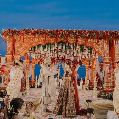 The Varmala ceremony under a magnificent floral mandap. We capture the entire scene to showcase the grandeur of the setup and the joy of the moment.