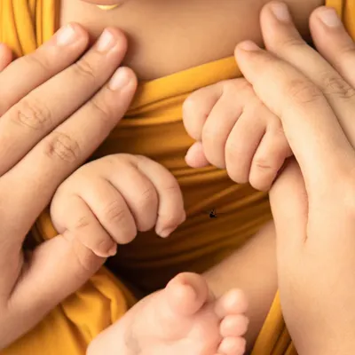 A close-up of a newborn's tiny hands and feet, gently held by their parents. Wrapped in a warm yellow cloth, this image captures the delicate and precious nature of a new life.