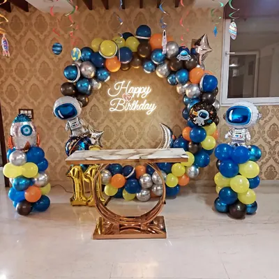 An out-of-this-world space-themed birthday party. This setup includes a balloon arch with planet and astronaut foil balloons, a neon sign, and a stylish cake table.