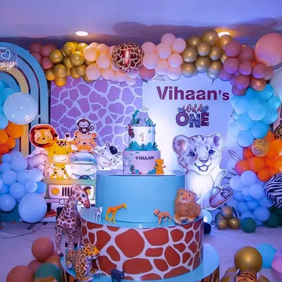 This safari theme is packed with details for a memorable first birthday. It includes a custom giraffe-print backdrop, multiple animal cutouts, a two-tiered cake stand, and a vibrant balloon garland.