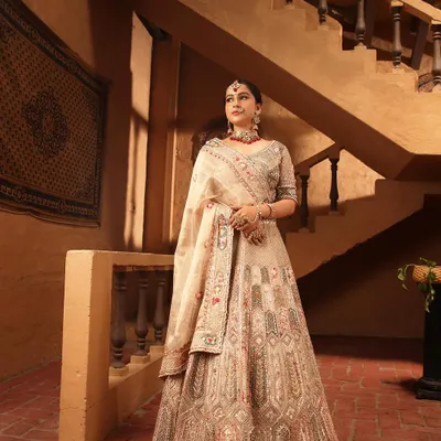 A full view of a stunning beige designer lehenga with intricate multi-color threadwork. This is a sophisticated and elegant choice for a reception or day wedding.