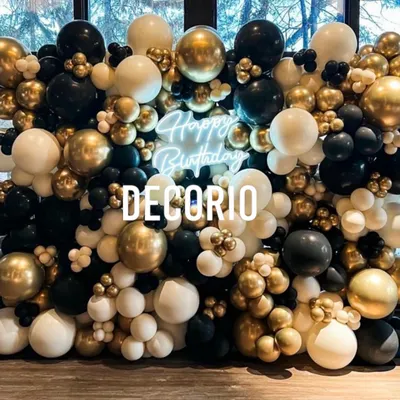 A stunning balloon wall in black, white, and chrome gold, creating a dense and luxurious backdrop. A 'Happy Birthday' neon sign is nestled within the balloons, adding a modern, glowing touch.