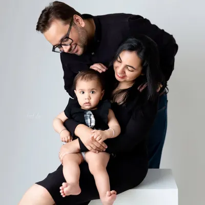 A loving family portrait with both parents smiling down at their baby, who is held securely in her mother's lap.