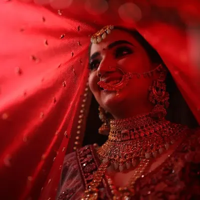 A bride's smile is her most beautiful accessory. Here, she is captured under her veil, with a makeup look centered on a classic red lip and glowing skin that radiates pure joy and confidence.