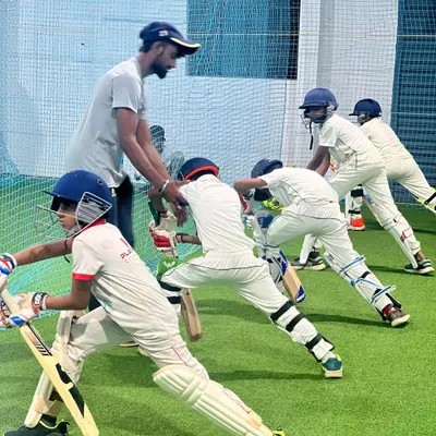 A coach provides hands-on guidance to a line of young batters in our indoor nets. This group drill focuses on establishing a solid, repeatable stance, which is the foundation of good batting.