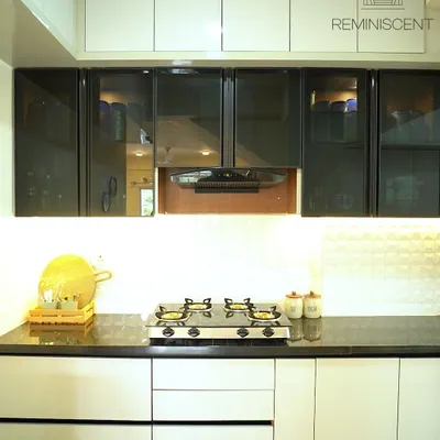 This kitchen showcases a sophisticated two-tone design with handleless glossy white upper cabinets and grey lower cabinets. The design is completed with glass-front display units and a clean, white backsplash, creating a bright and modern aesthetic.