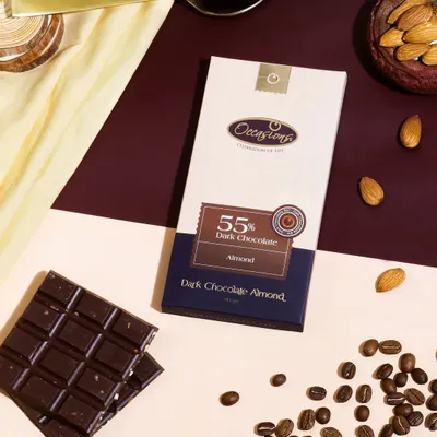 A stylish flat lay of a dark chocolate bar, composed with coffee beans, almonds, and contrasting colored backgrounds to tell a story of rich, complex flavors.