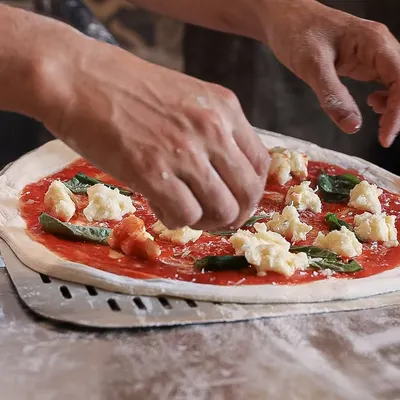 The making of a classic Margherita. Our pizzaiolo carefully places dollops of our fresh, handmade mozzarella on a base of rich tomato sauce and basil. It's an art form.