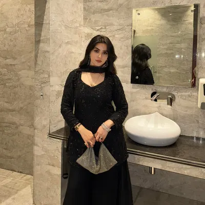 This is a full-length shot of a stunning black sequined ethnic outfit. The luxurious marble background of the washroom complements the outfit's elegance, making it perfect for showcasing high-end party wear.